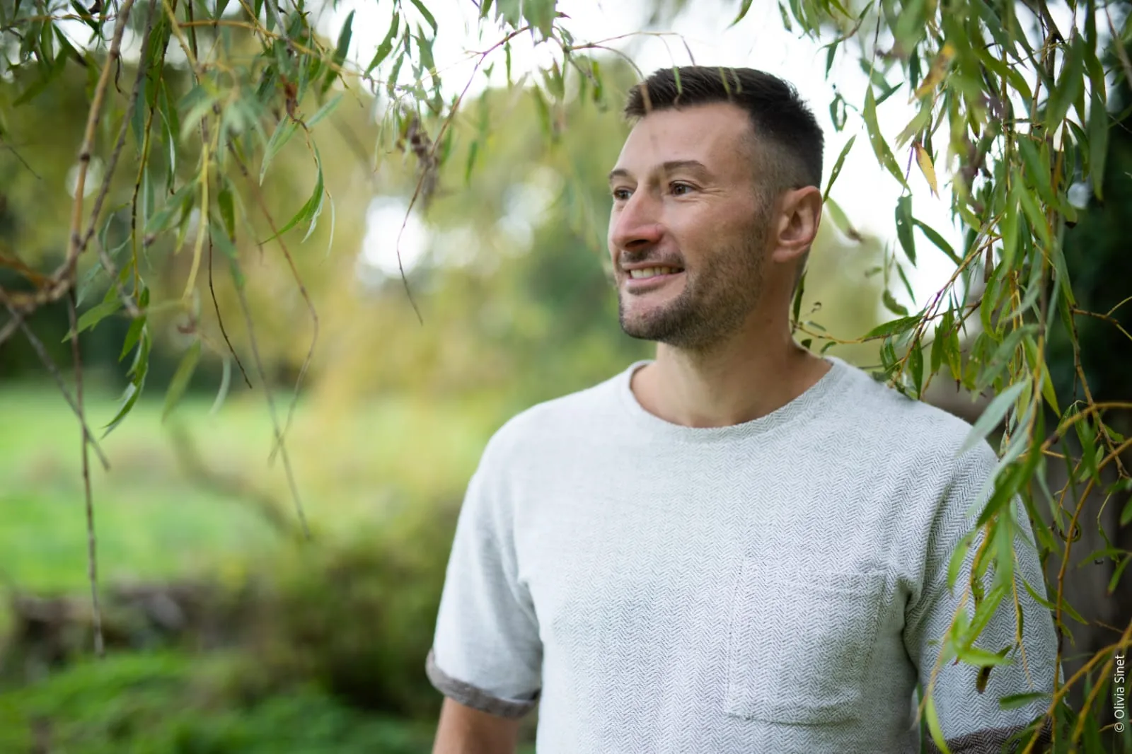 Damien Doussot souriant sous les branches d'un saule, dans la nature